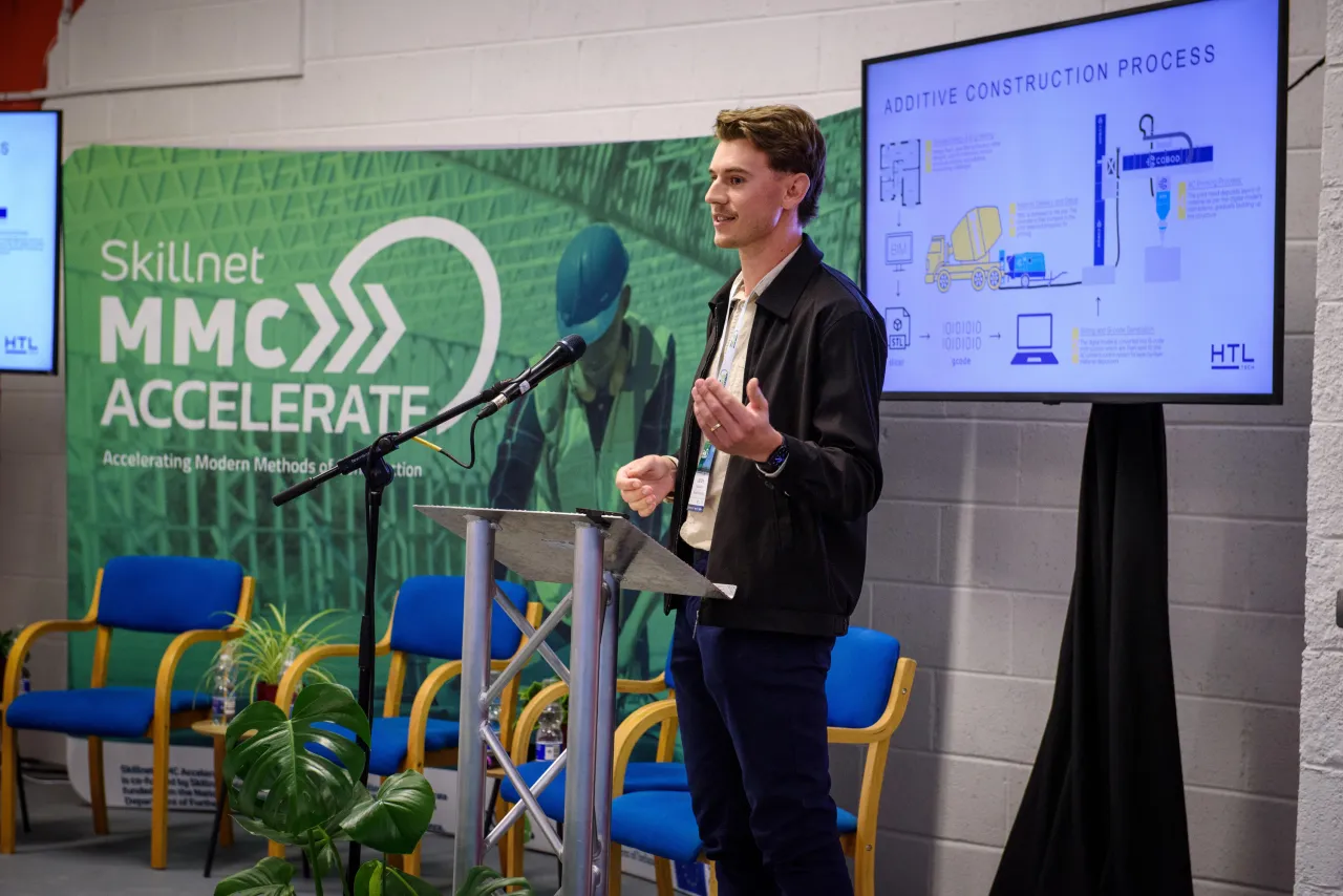 Person presenting at MMC Accelerate event with digital screen displaying data beside them.