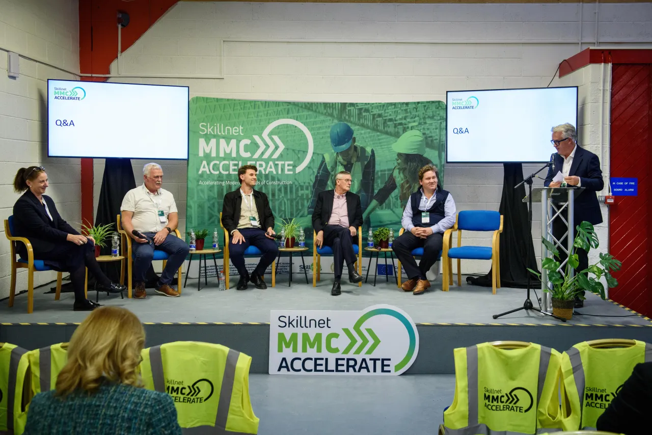 Panel discussion with several people seated on stage at a "Green Accelerator" event, featuring presentation screens.