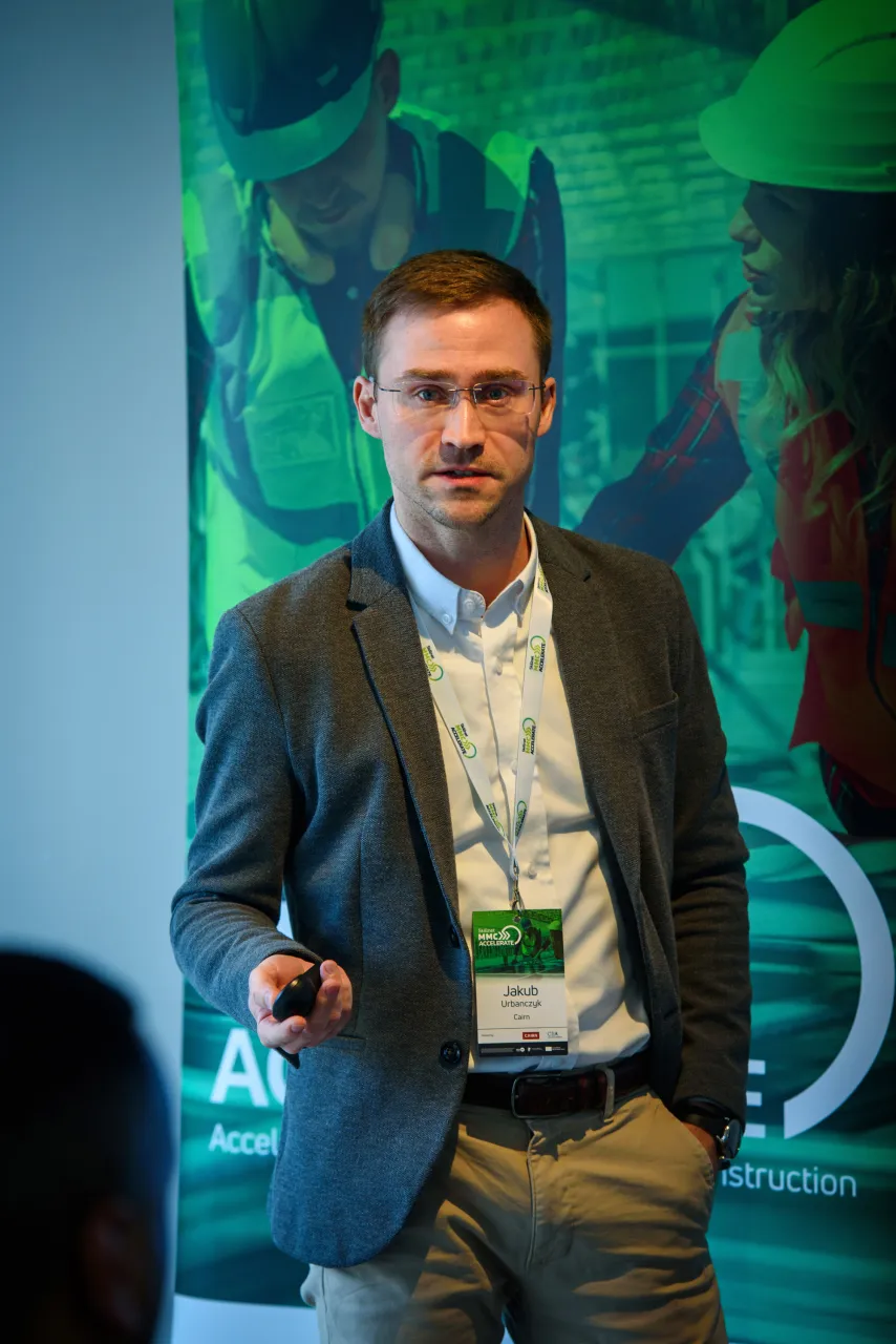 A person in business attire speaking at a podium with a blue-green digital background.