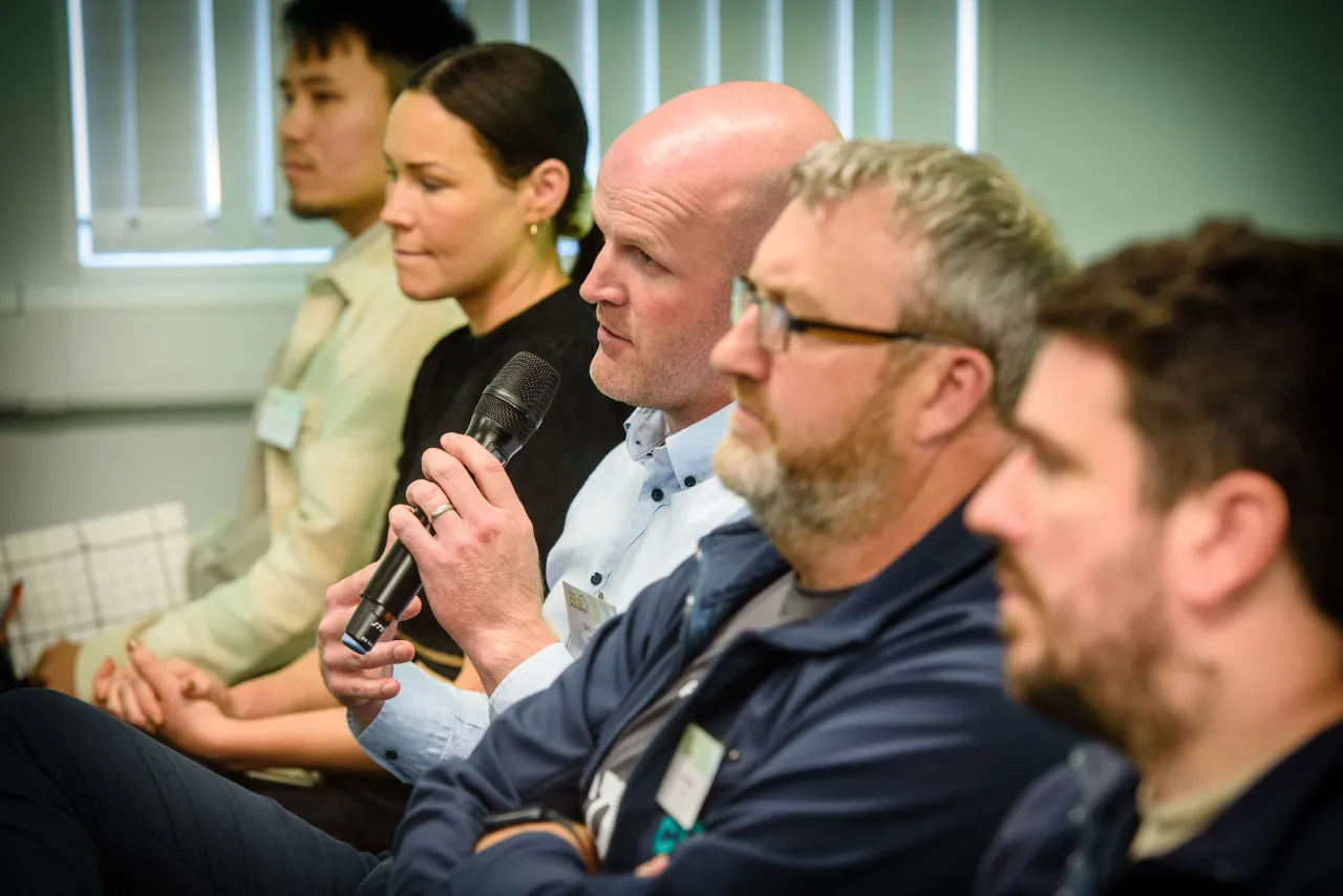 A group of people sitting in a row, attending what appears to be a meeting or presentation.
