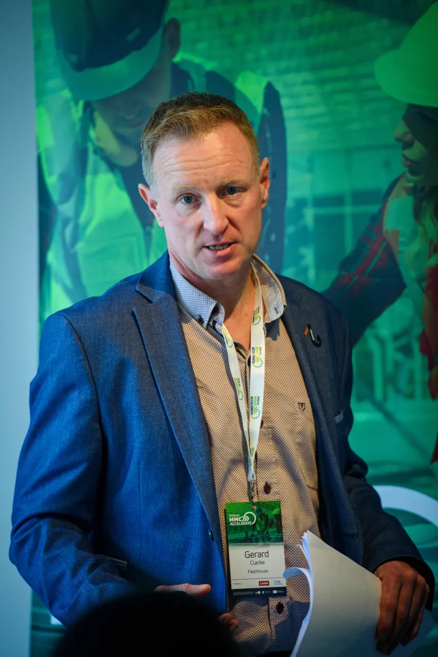 A person in a blue suit speaking at a podium against a green backdrop.