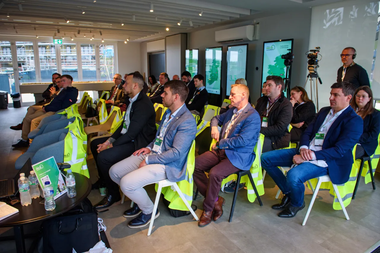 People seated in a semicircle on green chairs at a professional gathering or workshop.