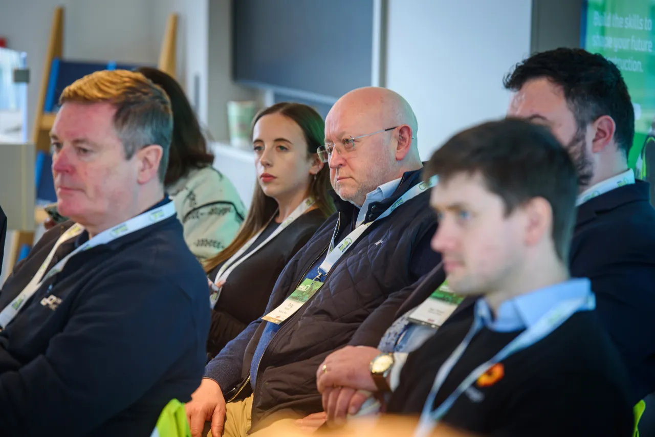 Row of attendees seated at a conference, focusing on a presentation off-camera.