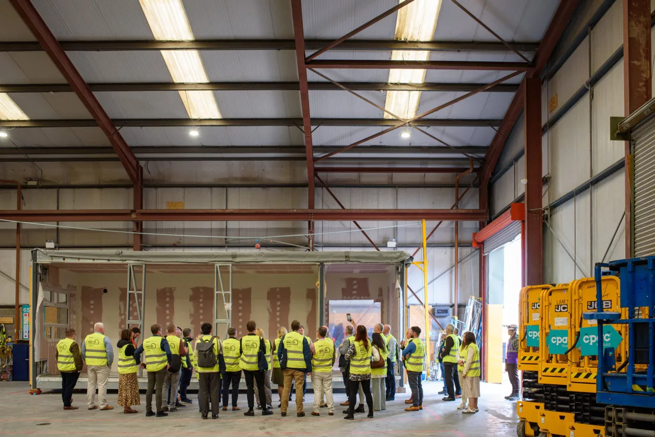 Group of workers in high-visibility vests gathered inside a large industrial warehouse with stacked containers.