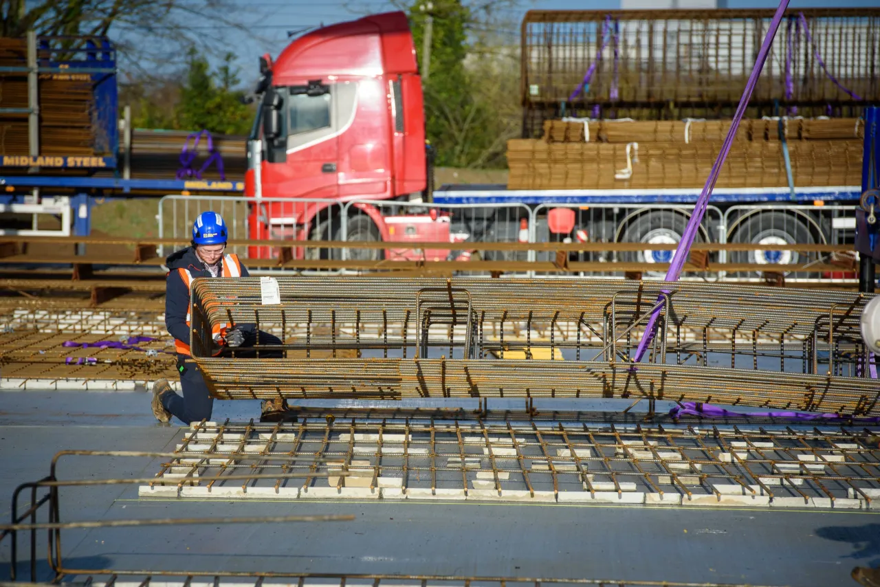 Construction workers assembling rebar on a site with a red truck visible in the background.