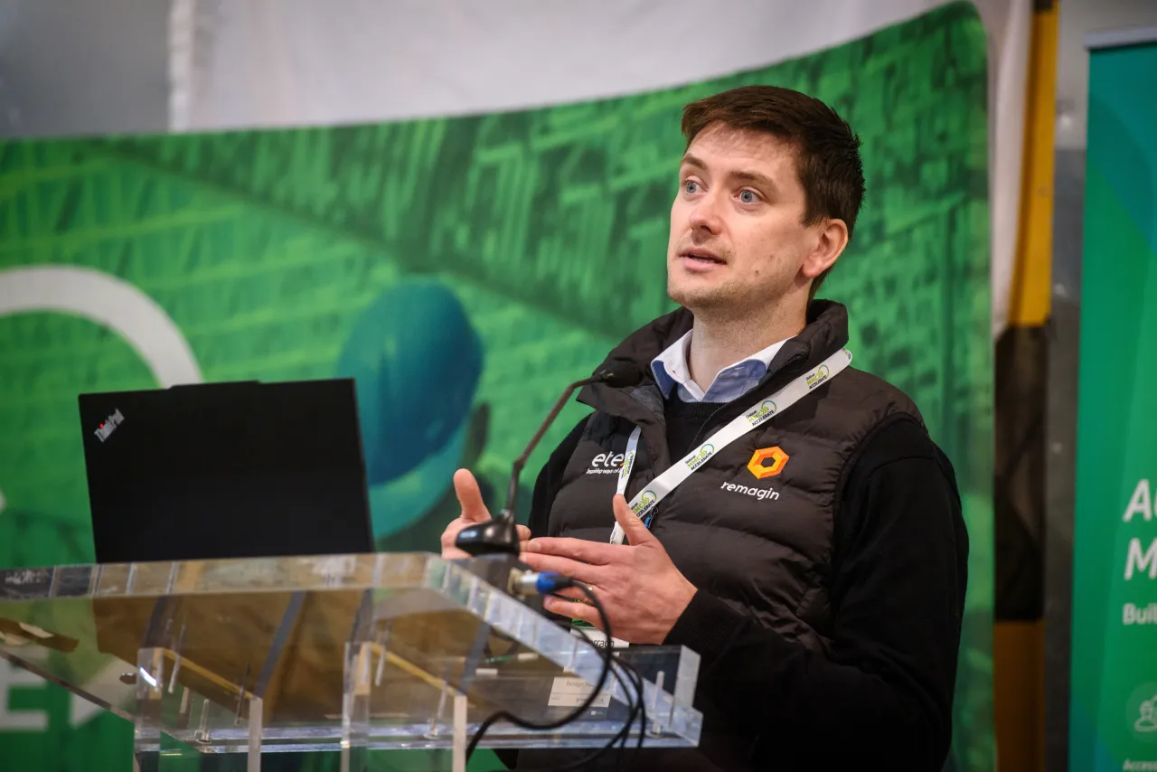 Speaker at a podium with a laptop in front of a green backdrop.