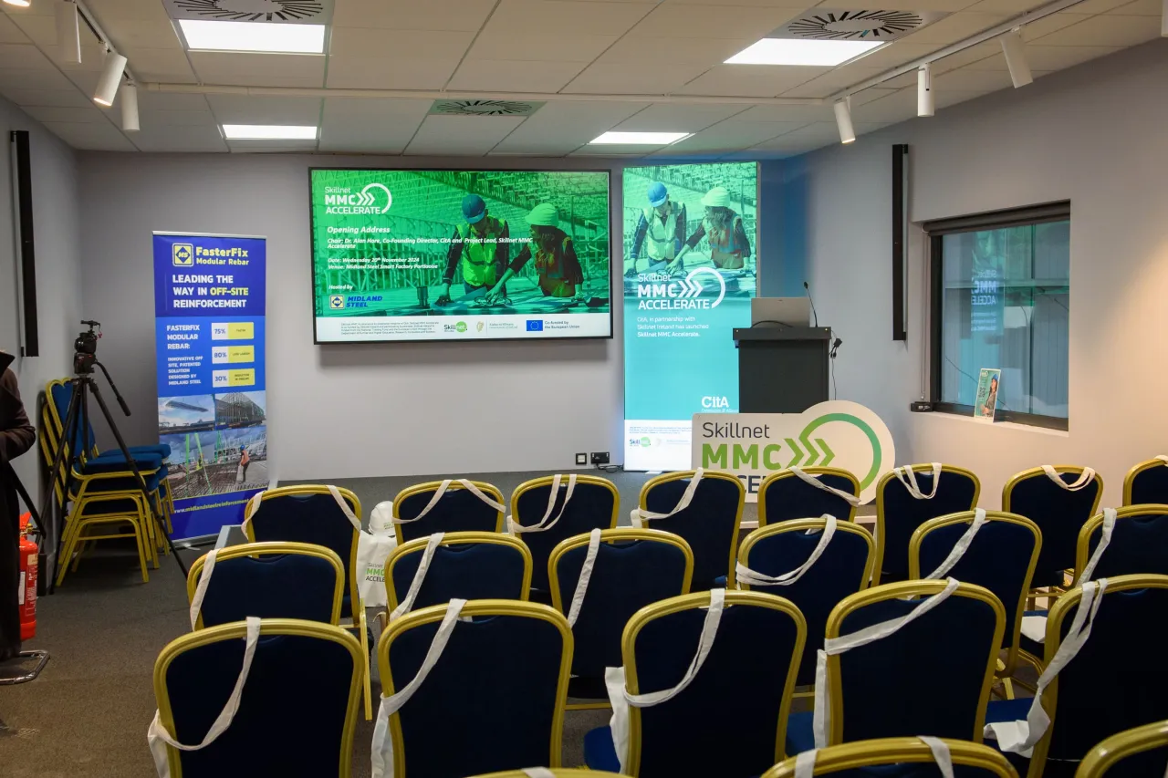 Empty conference room with rows of chairs facing a large screen displaying presentation slides.