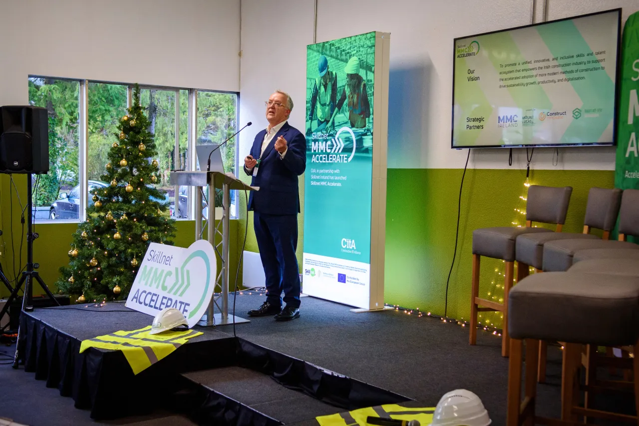 Person speaking at a podium in a bright room with green accents and Christmas decorations.