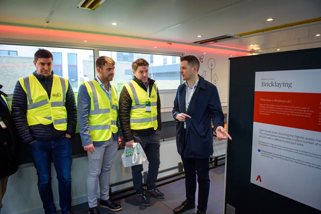 Three construction workers in yellow vests standing with a businessman viewing a presentation board.