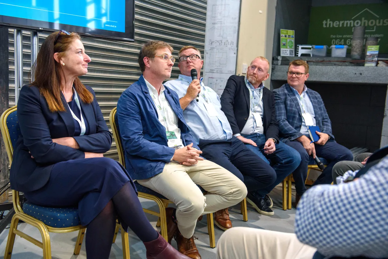Panel discussion with four professionals seated on stools at a business event, blue backdrop.