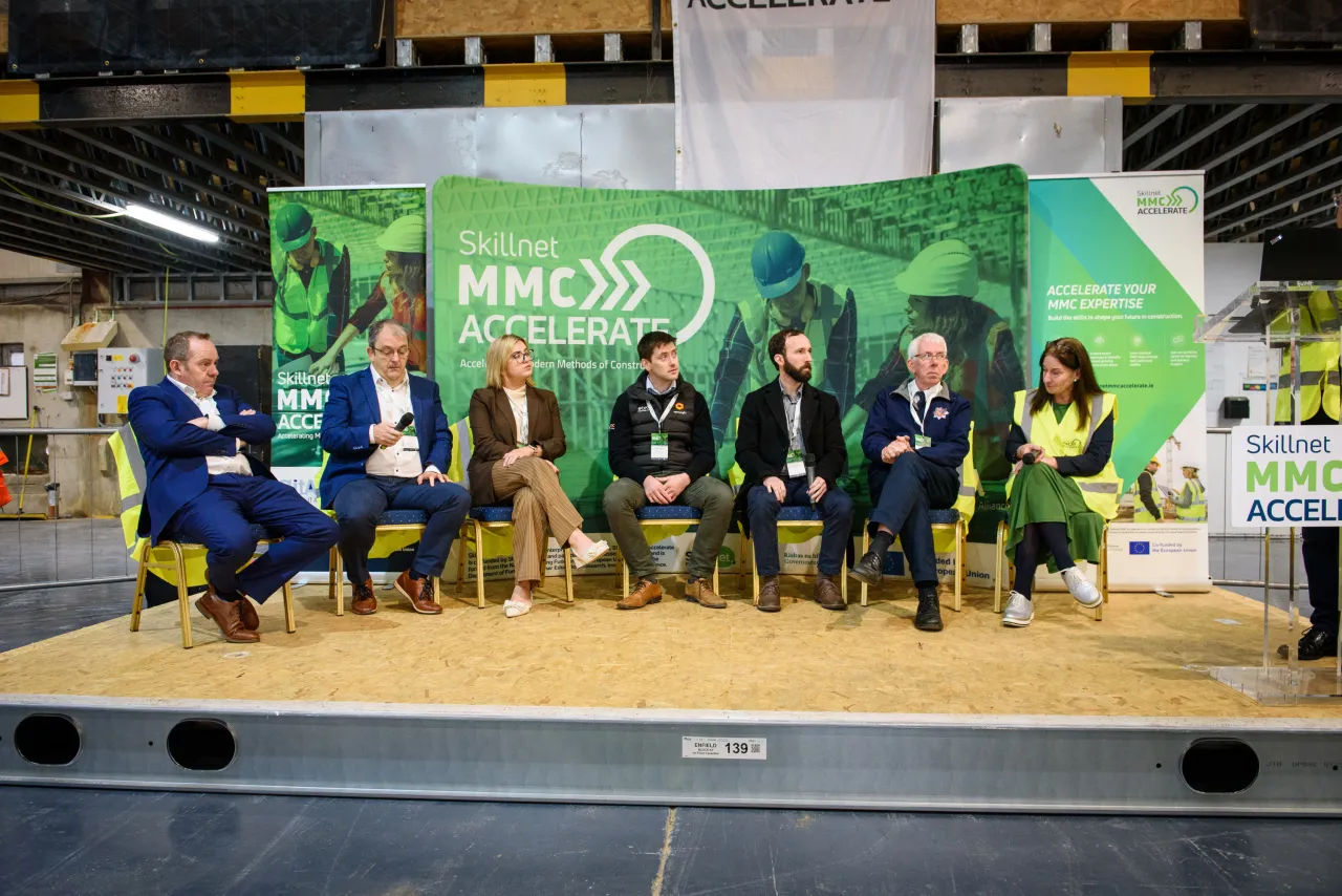 Panel of speakers seated on a stage with a green backdrop featuring a "Green Deal" logo.