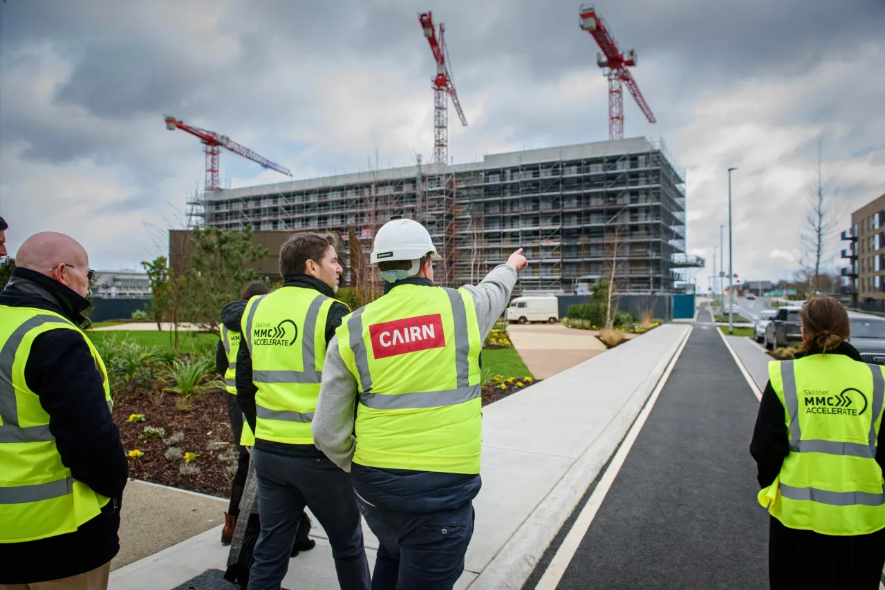 Construction workers in high-visibility vests overlooking a building site with cranes and scaffolding.