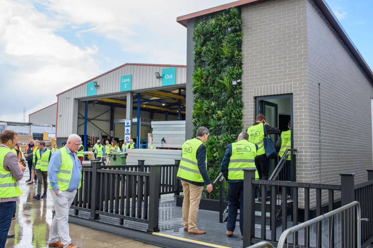 A group of people in neon safety vests standing outside a modern building with a living plant wall.