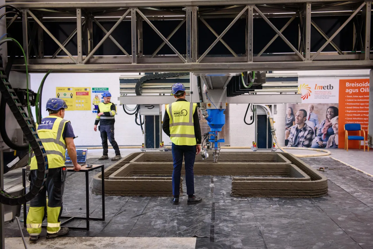 Construction workers at a site with colorful panel walls showing people illustrations in background.