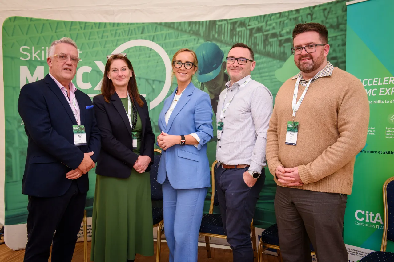 Group of five professionals standing together in front of a green event backdrop.
