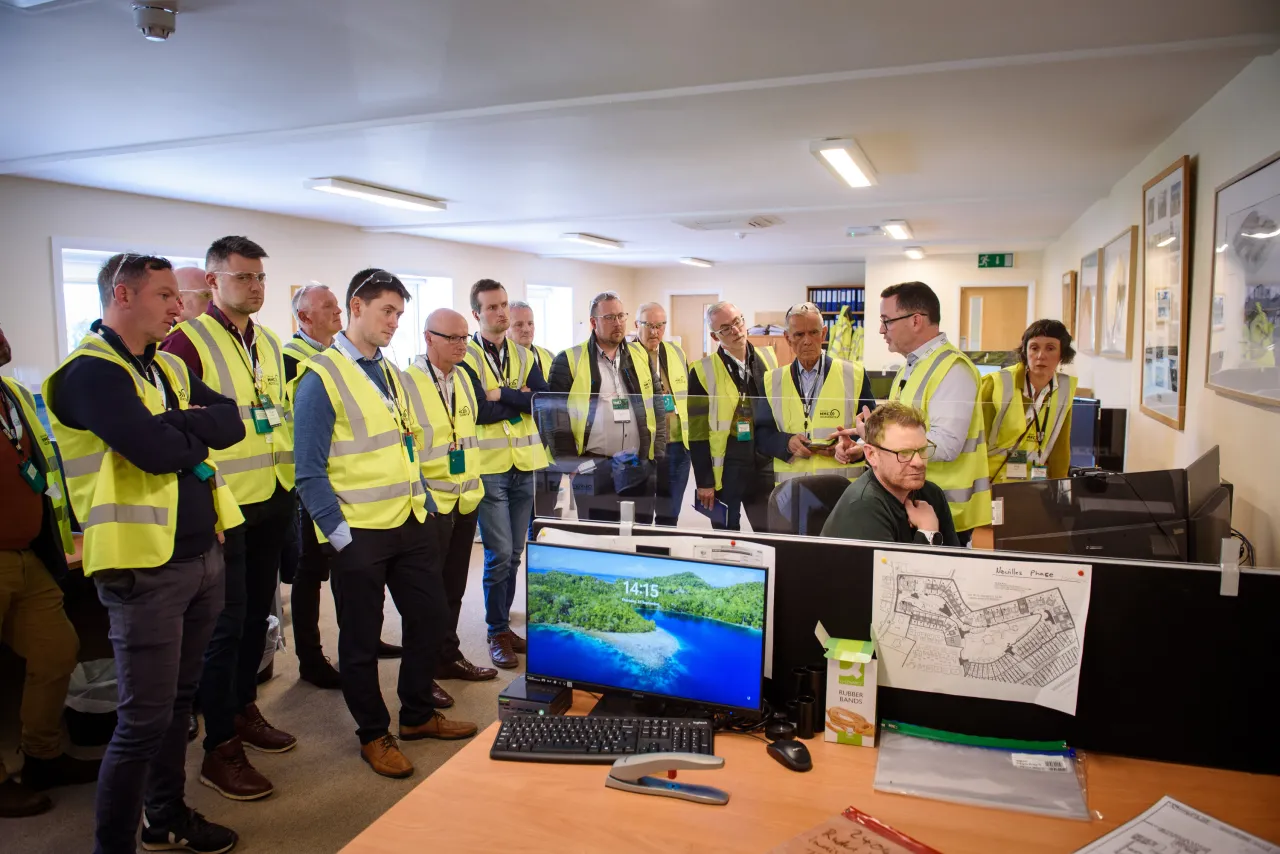 Group of people in safety vests gathered in an office, viewing a monitor displaying a map.