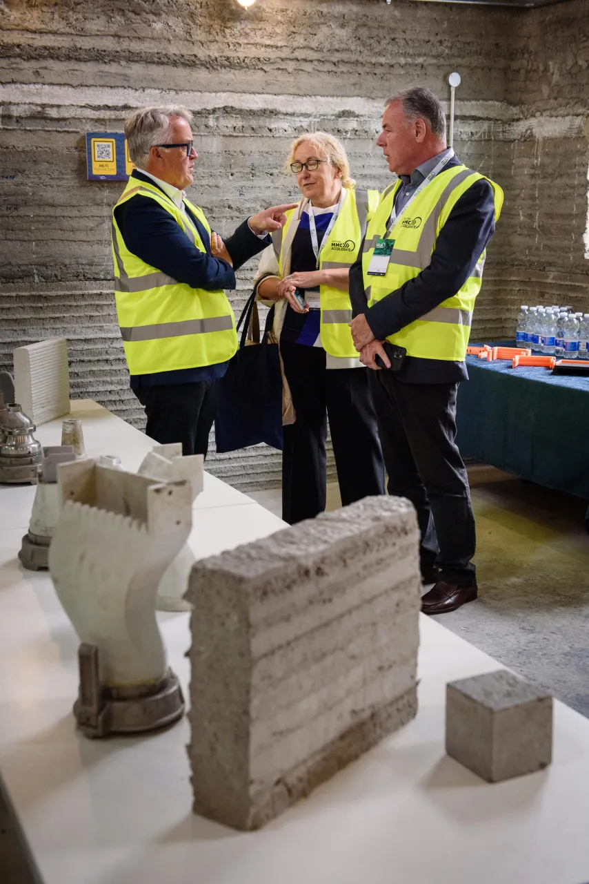 Three people in safety vests examining architectural stonework pieces on a table.