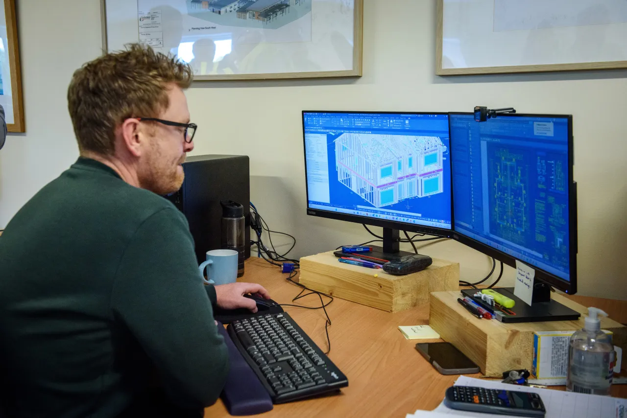 A person in a green sweater working at a desk with multiple computer monitors.