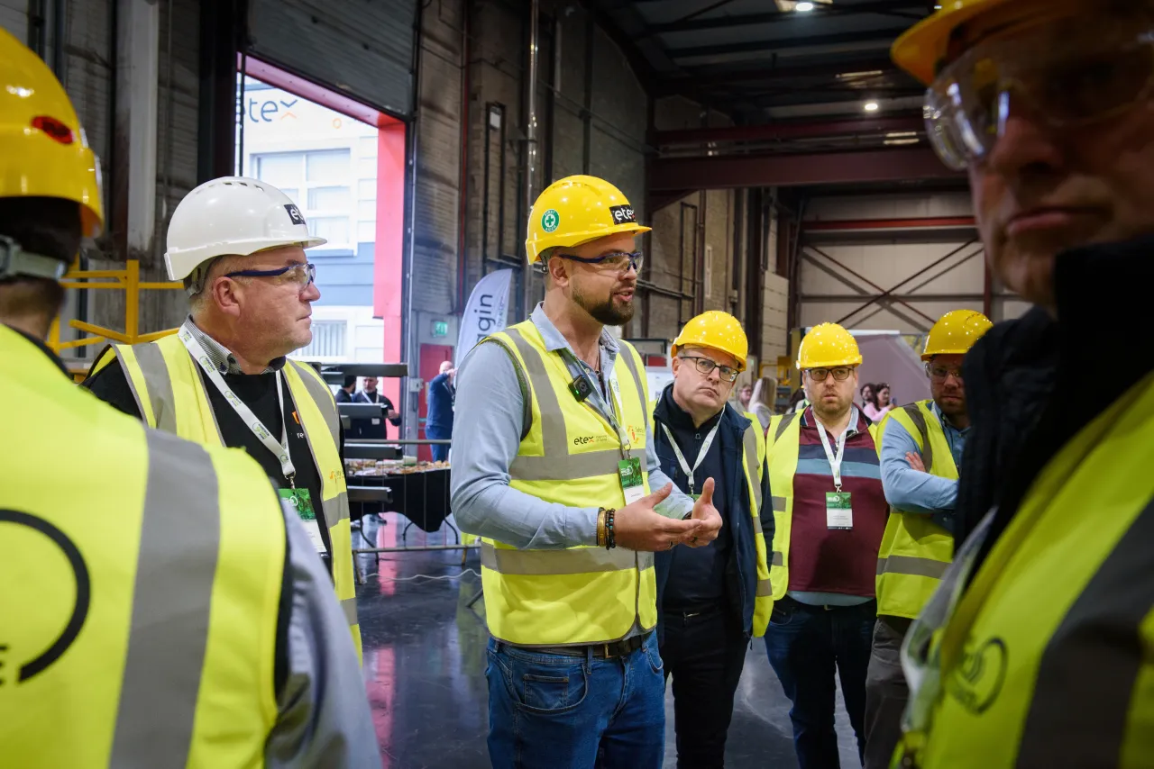 Group of workers in yellow hard hats and safety vests standing in an industrial facility.