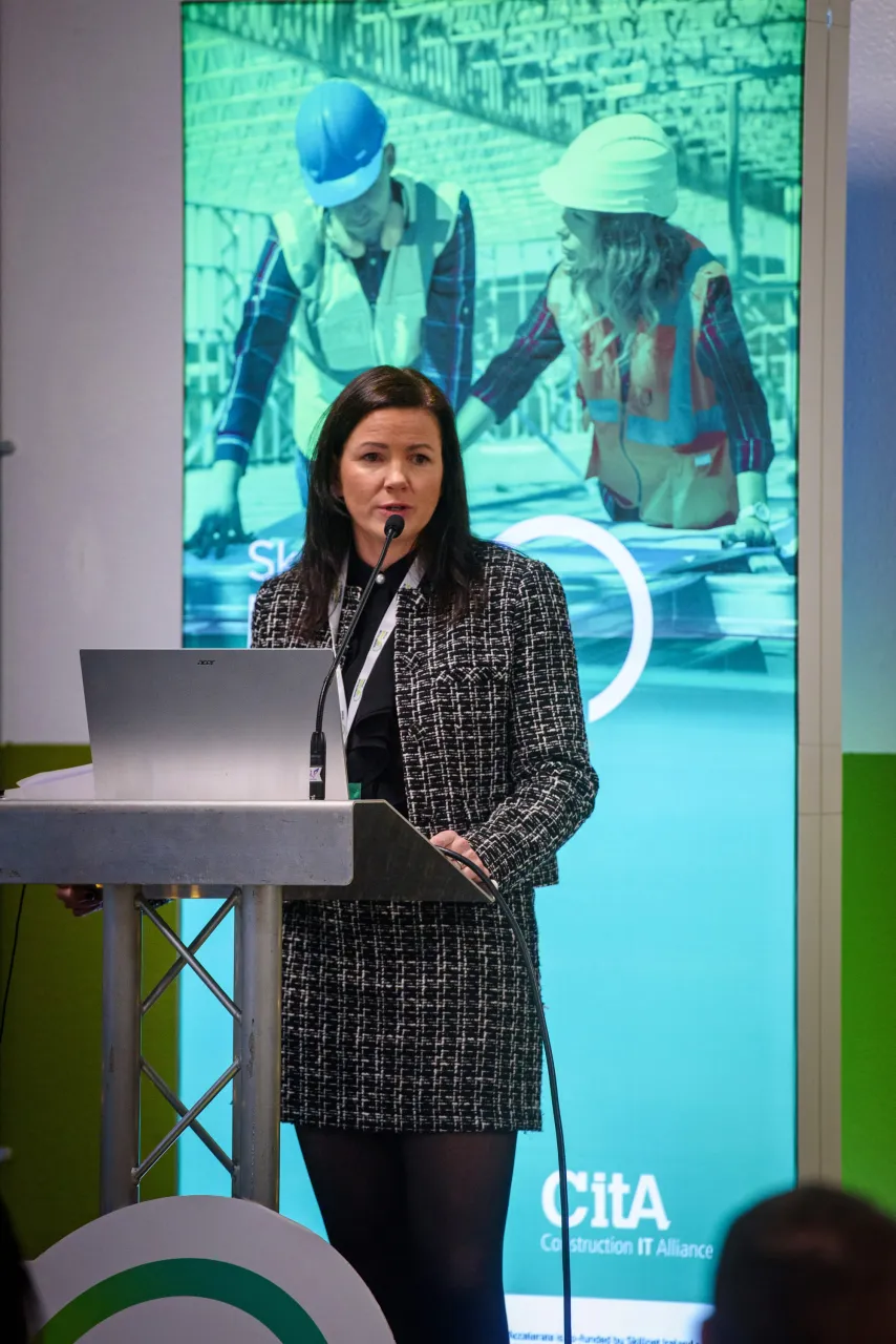 A person in a checkered jacket standing in front of a projected presentation screen.