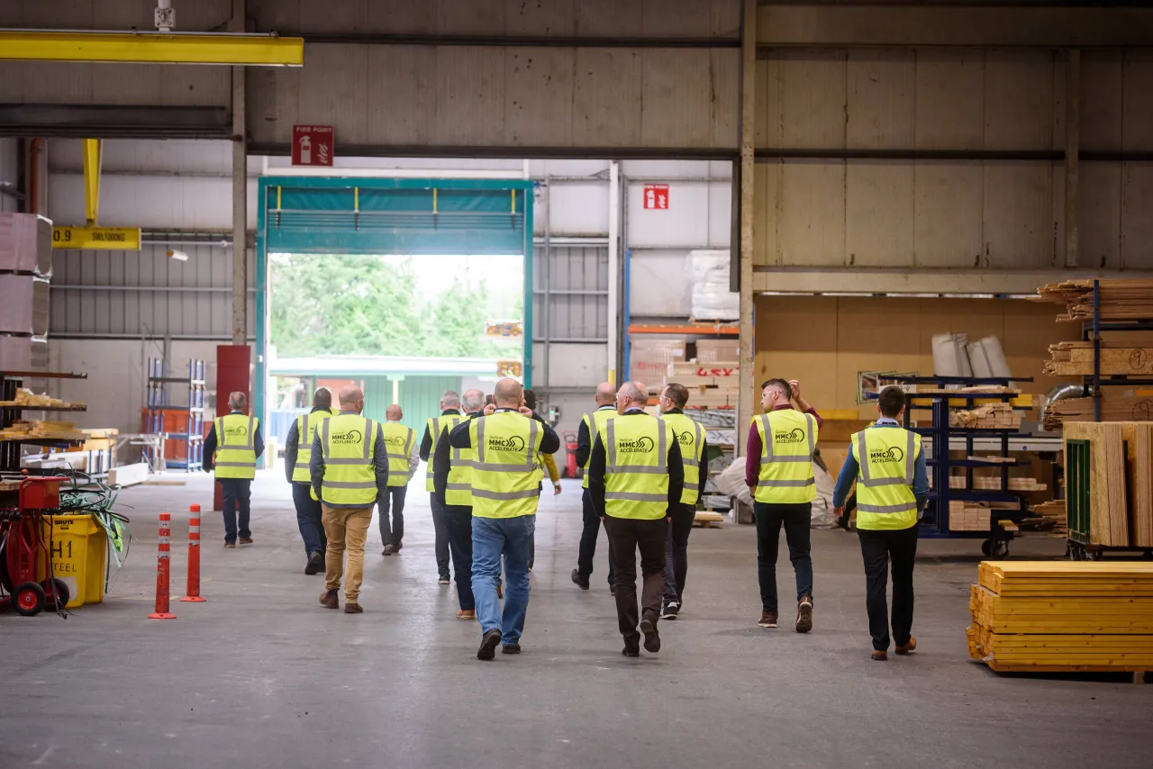 Workers in high-visibility safety vests walking through a warehouse or industrial facility.