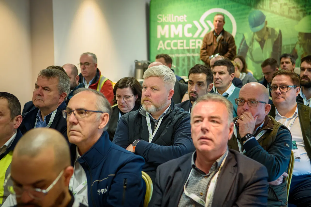 Attendees gathered at a conference or meeting with green corporate branding on display.