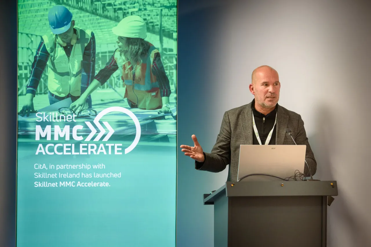 Person in business attire presenting at a conference with a MRO event banner visible.