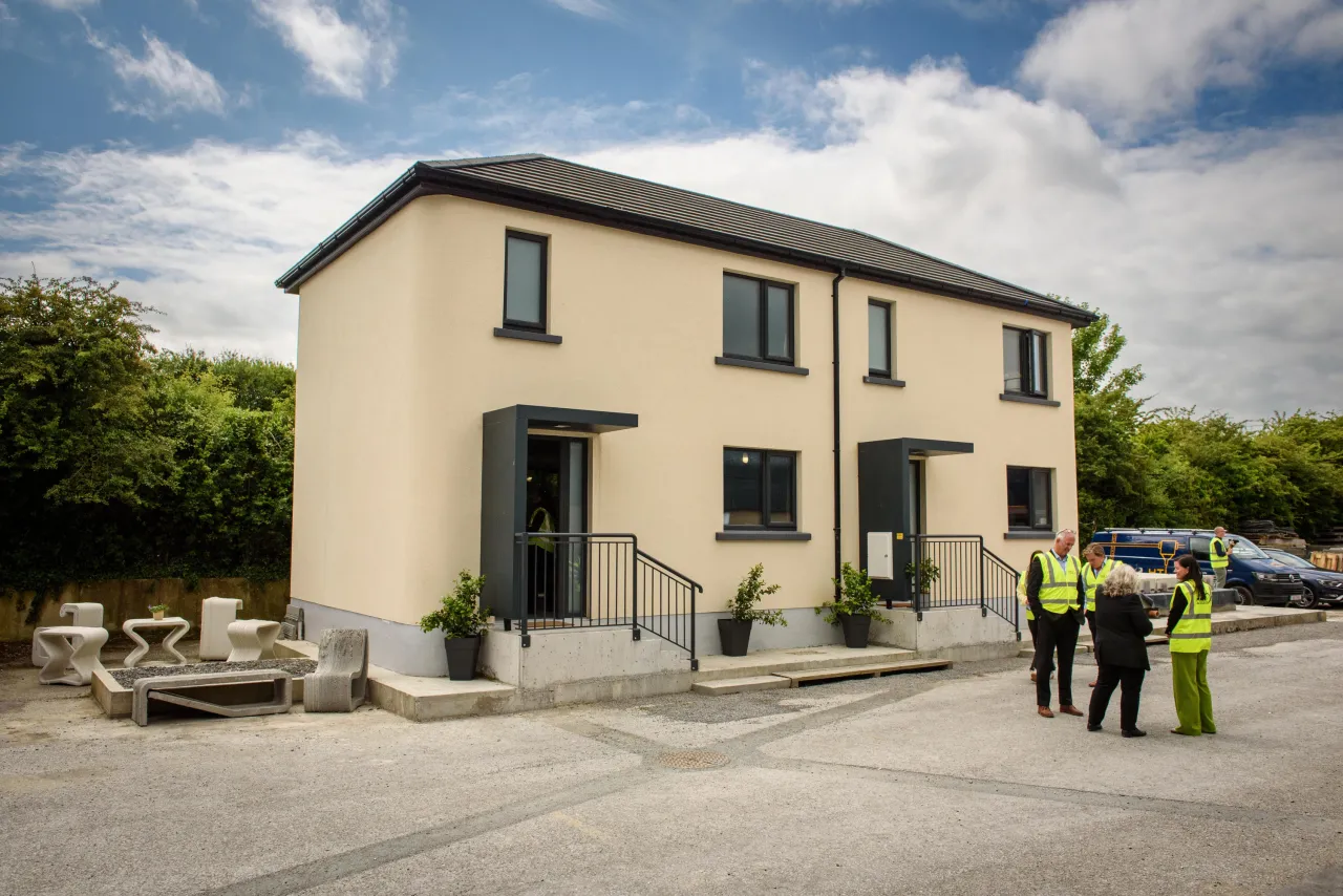 New beige semi-detached house with workers in hi-vis vests standing in the driveway.