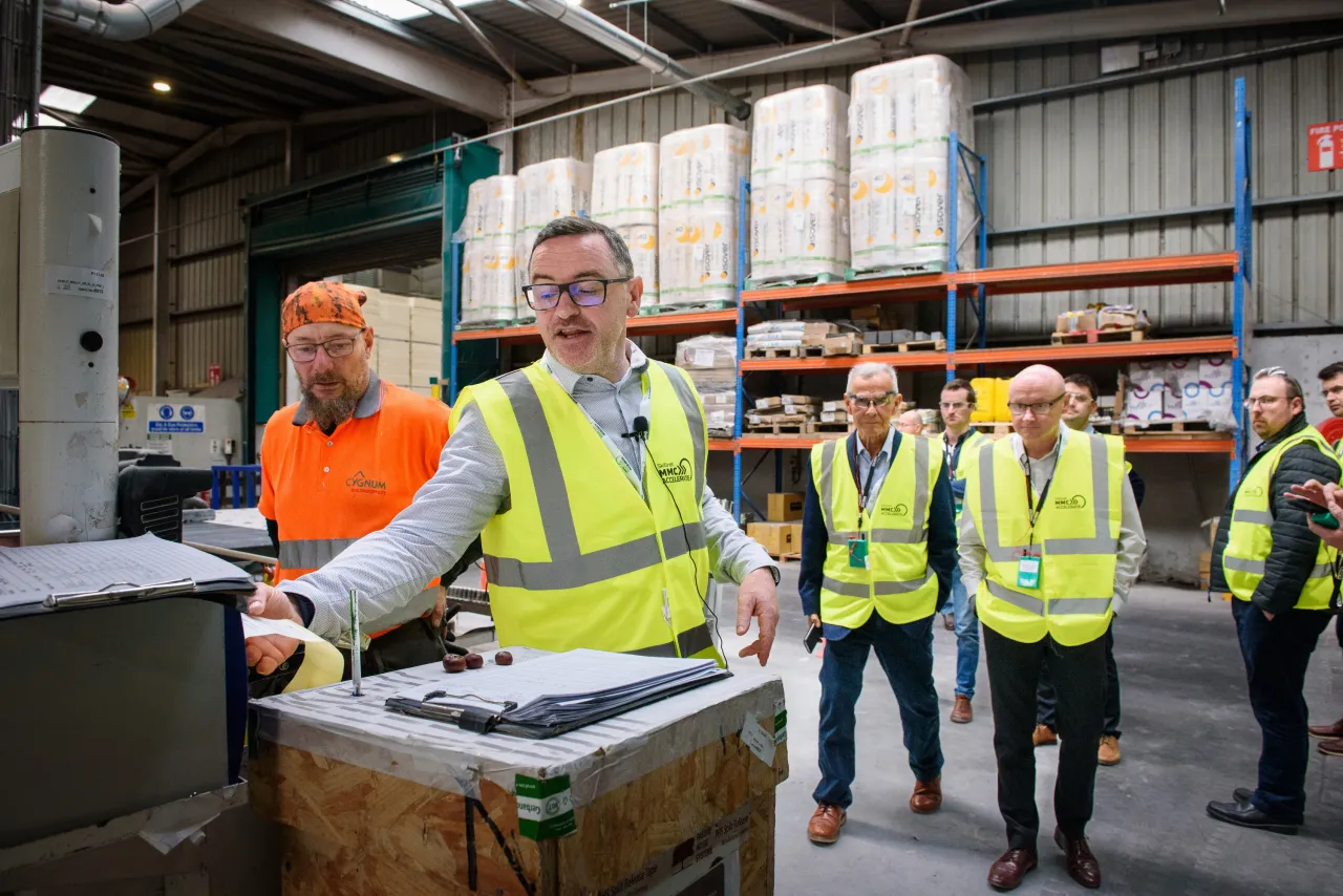 Workers in high-visibility vests at a warehouse facility with shelving units in the background.