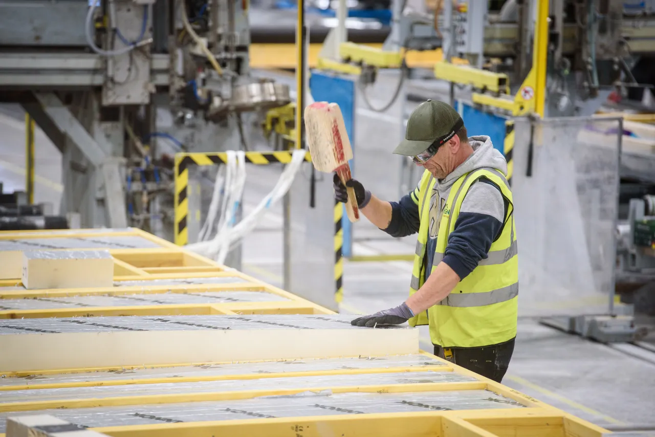 Factory worker in safety gear inspecting yellow industrial materials on production line.