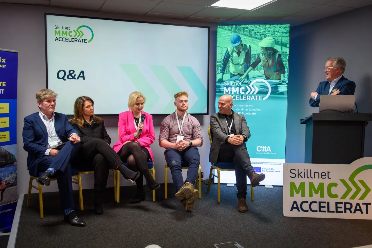 Panel discussion with four speakers seated on stage and a moderator standing at a podium.