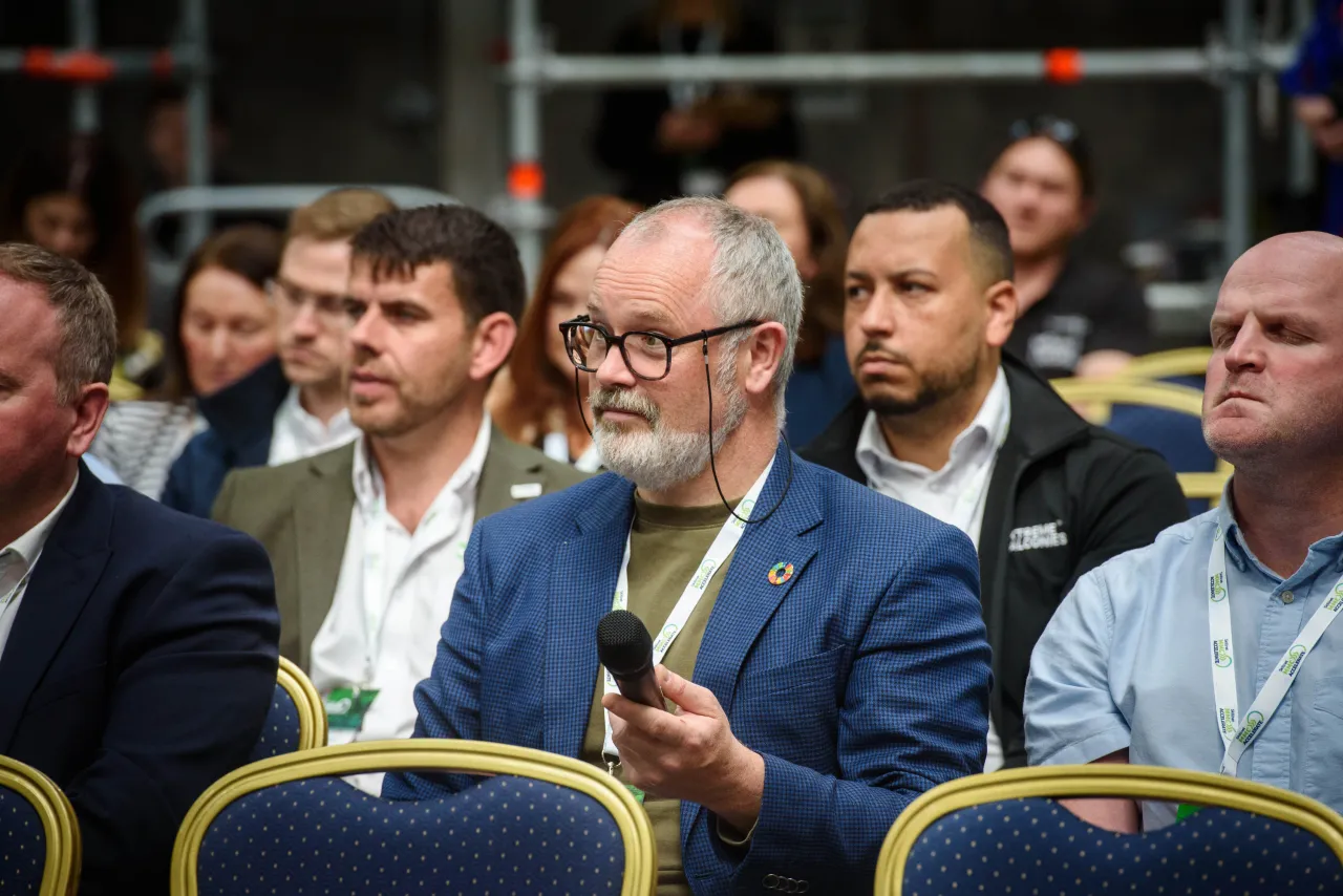 Men in suits sitting in a row at a formal event, with one wearing glasses in the center.