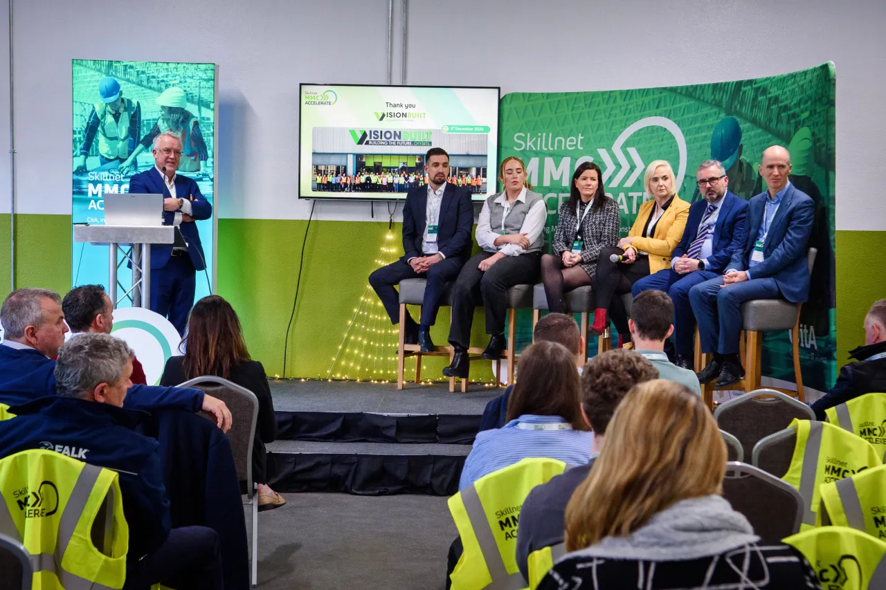 Panel discussion with speakers seated on stage with green backdrop at a professional event.