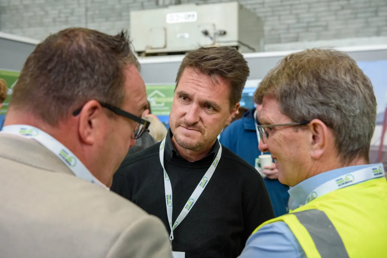 Three professionals in discussion, one wearing safety vest, in an industrial setting.