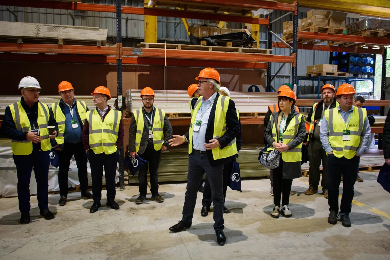 Workers in safety gear and hard hats standing in a warehouse with industrial shelving.