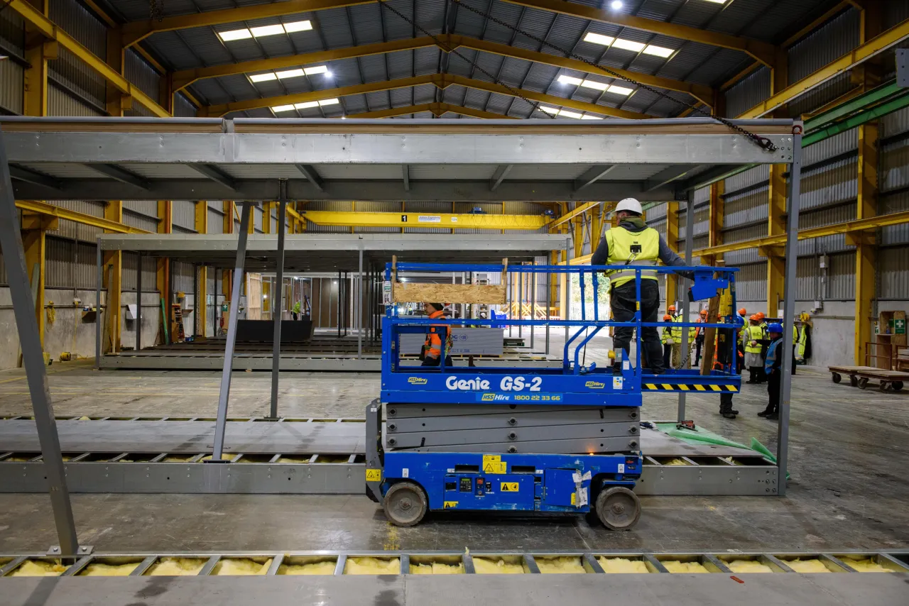 A worker on a blue scissor lift inside a large industrial warehouse facility.