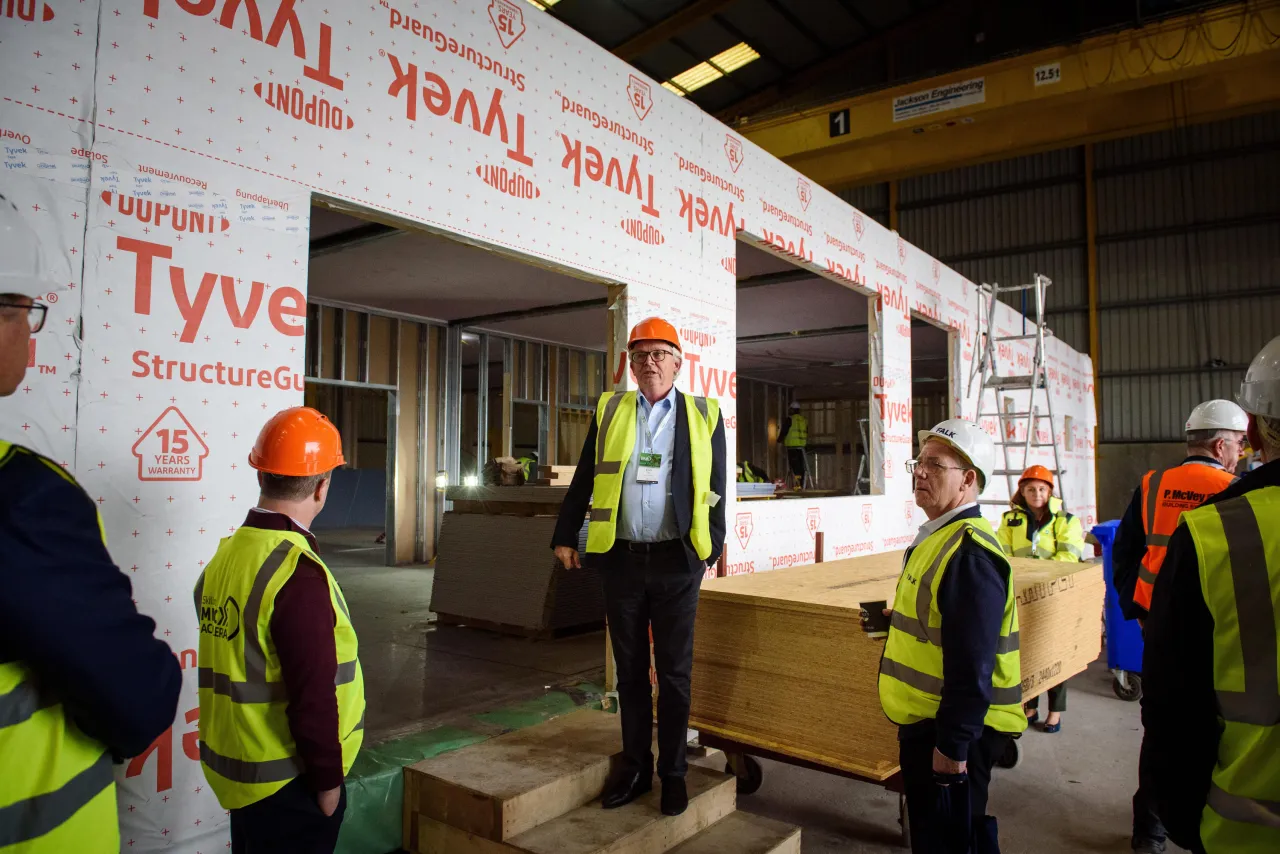Construction workers in high-visibility vests examining a prefabricated wall with Tyvek insulation material.