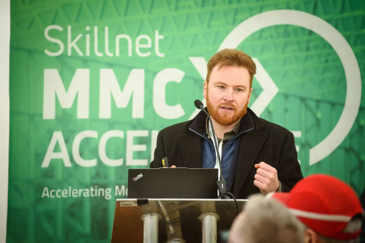 Young bearded man speaking at a podium in front of a green Skillnet MMC Academy banner.