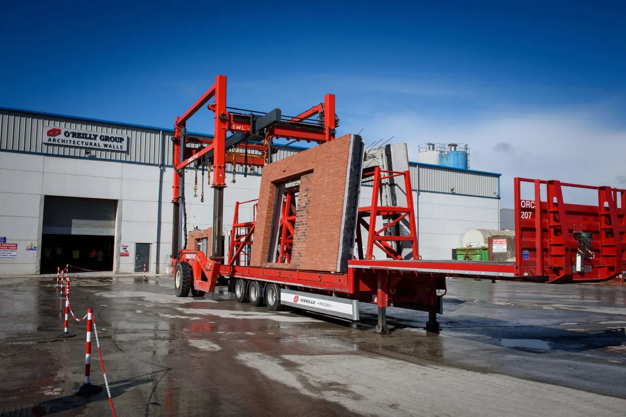 Red truck trailer with a hydraulic unloading system tilting cargo at an industrial warehouse.