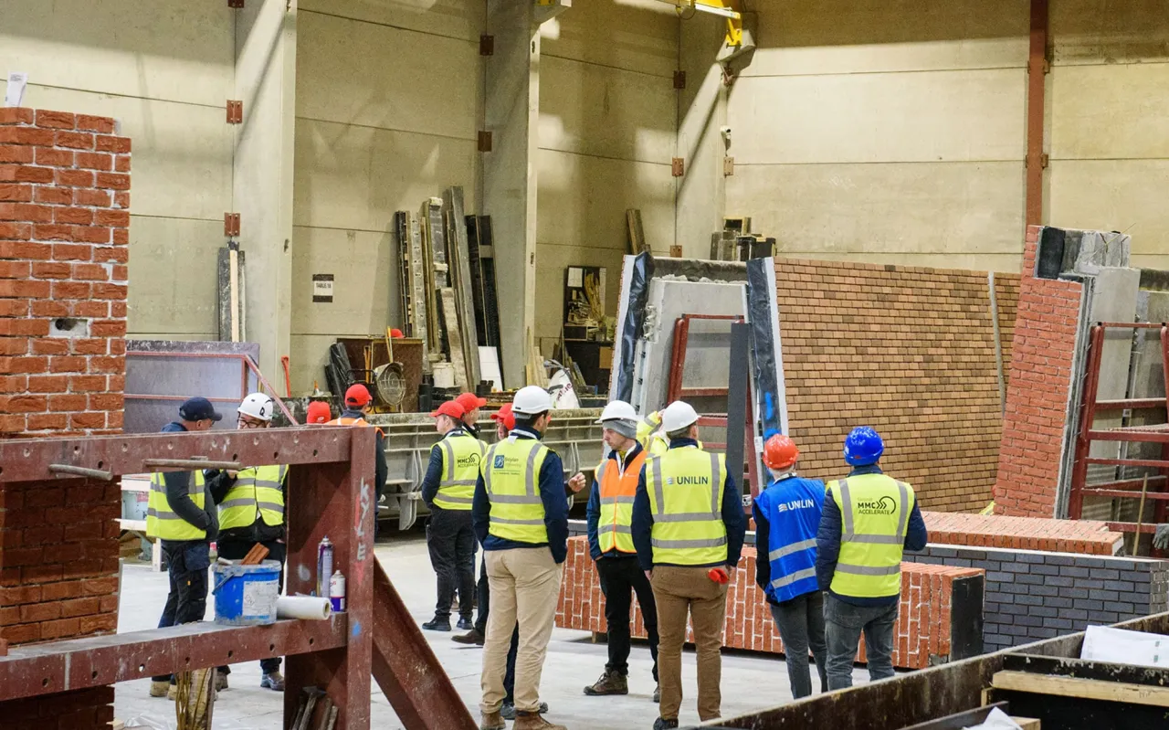 Group of workers in high-visibility vests observing construction work inside an industrial building.