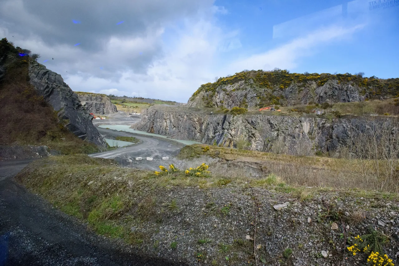 Rocky limestone quarry with steep cliff faces under a partly cloudy sky.