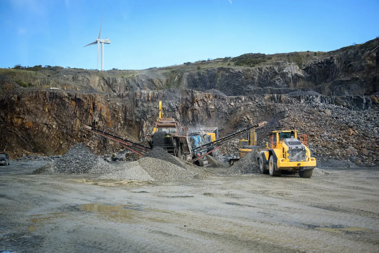 Heavy machinery working at an open-pit quarry with rocky terrain and overcast skies.