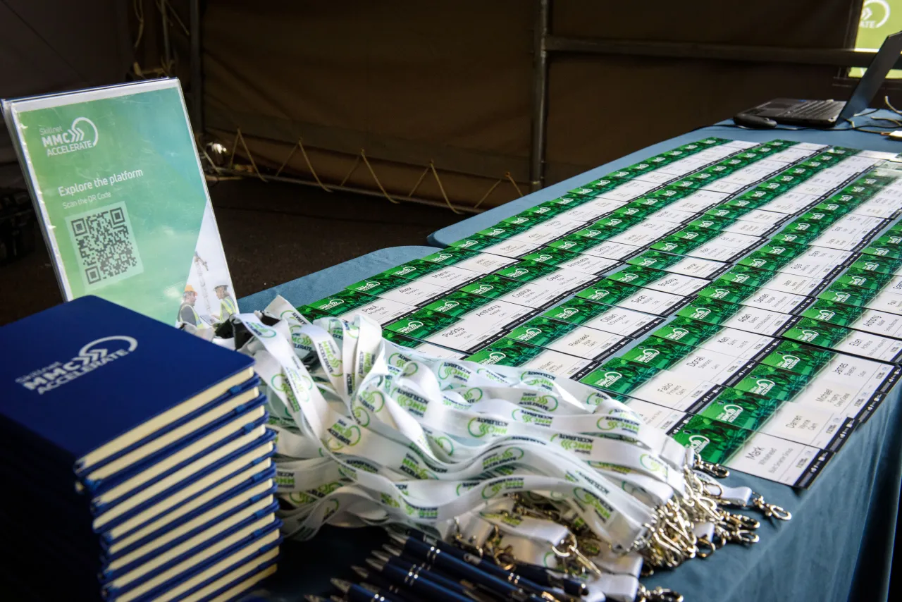 Table displaying rows of green and white medals, lanyards, and stacked booklets at an outdoor event.