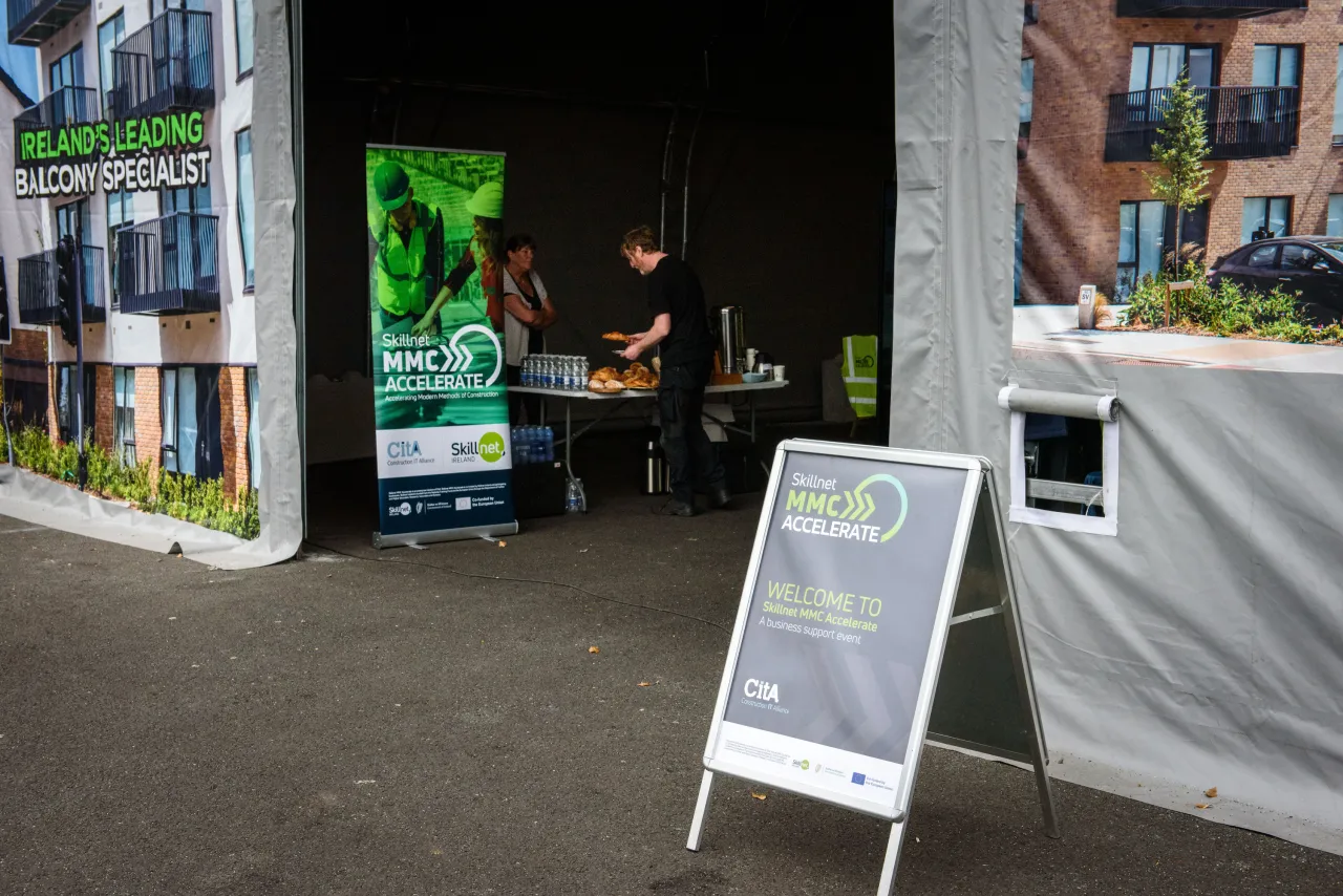 Outdoor event booth with green signage and a person working at a table under a canopy.