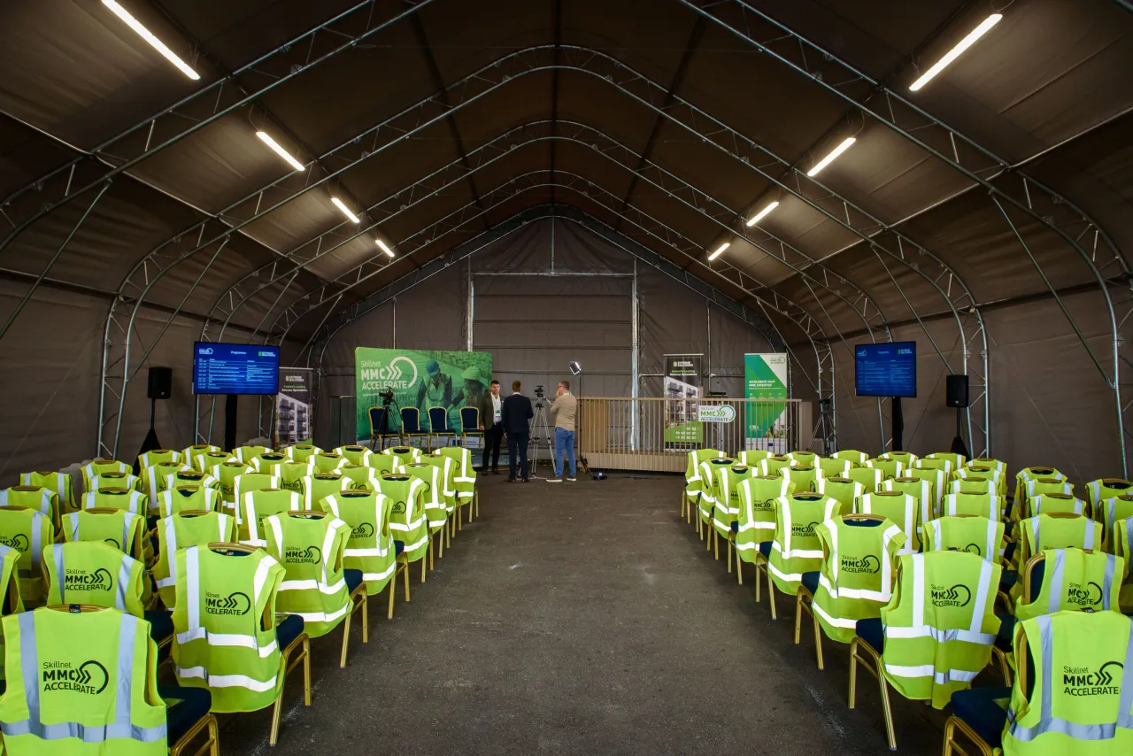 Rows of yellow high-visibility vests on chairs inside a large tent venue set up for a safety briefing.