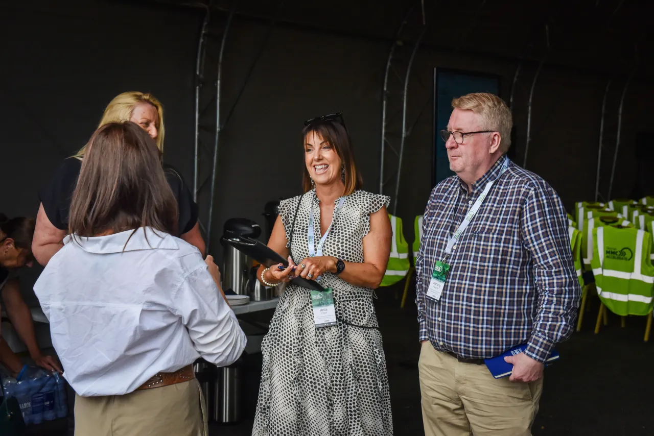 Three people engaged in conversation at an indoor event, one wearing a green lanyard.