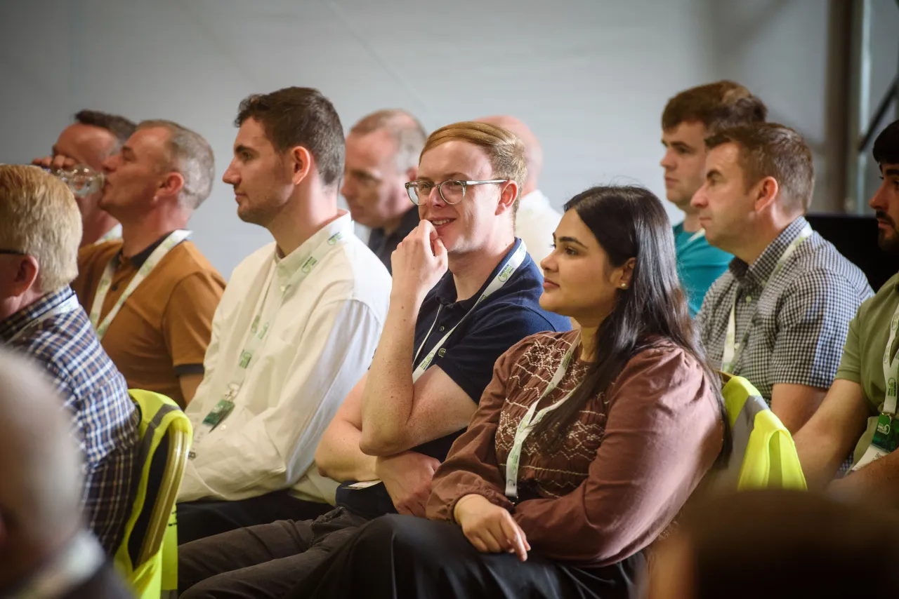 A diverse group of adults seated in rows, attentively listening at an indoor event or meeting.