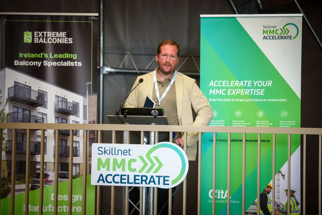 Man speaking at a podium beside a Skillnet MMC Accelerate banner at an indoor event.
