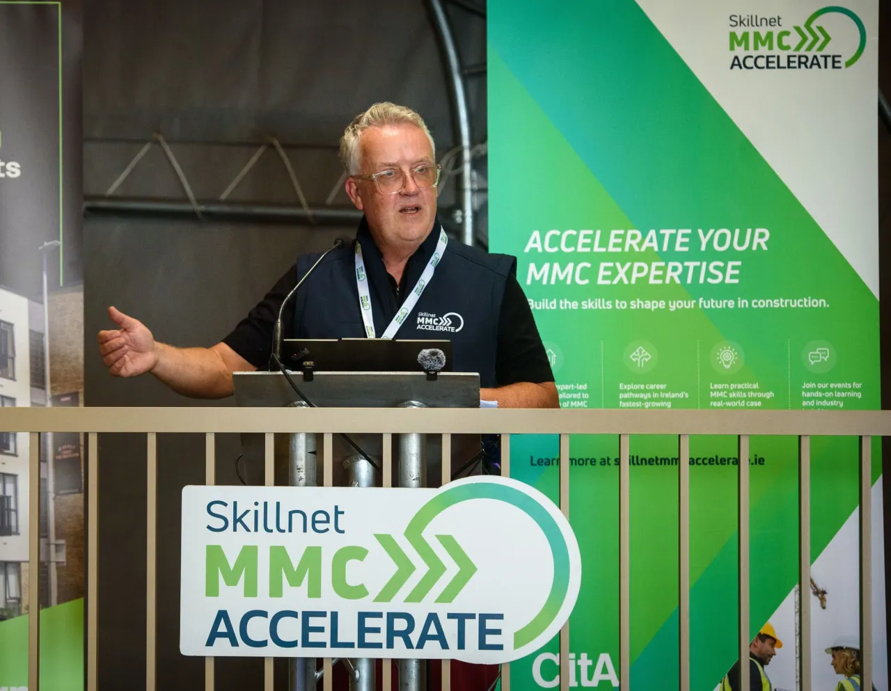 Person speaking at a Skillnet MMC Accelerate event podium with green promotional banners.