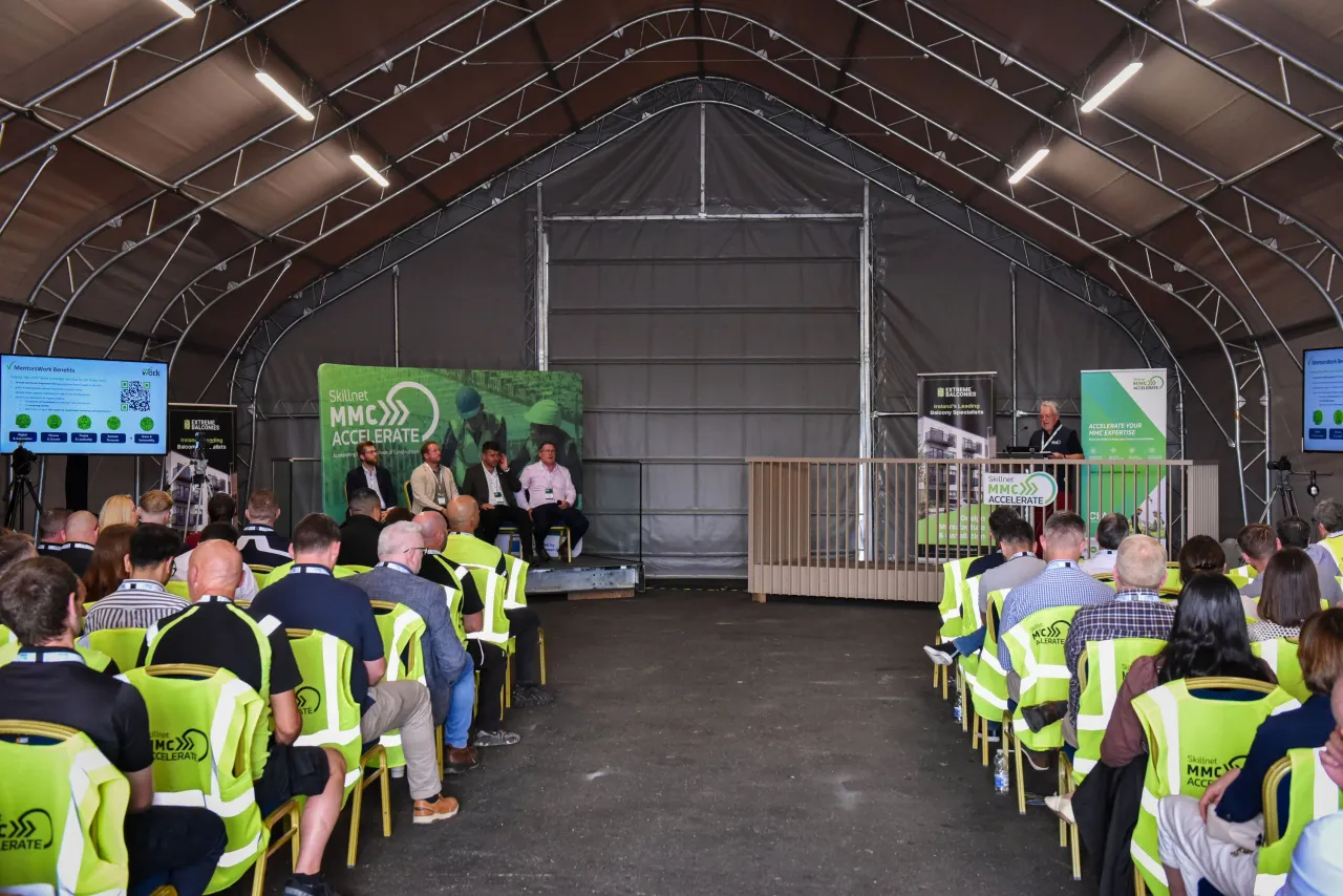 Workers in high-visibility vests attending a presentation inside a large industrial shed.